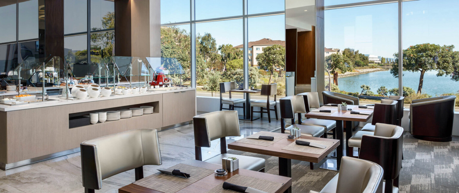 a food service buffet station and dining area overlooking trees and a bay following Marriott brand architecture