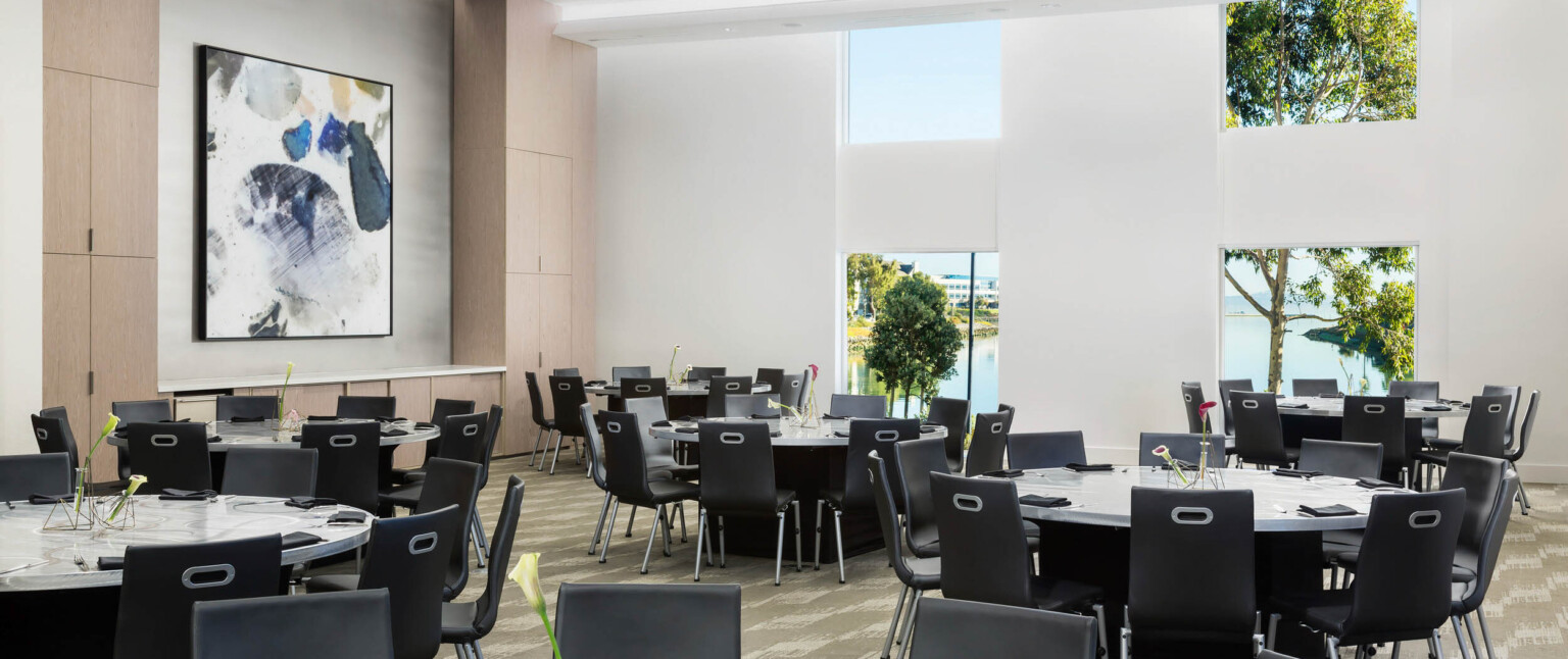 a ballroom with black chairs round tables and square windows