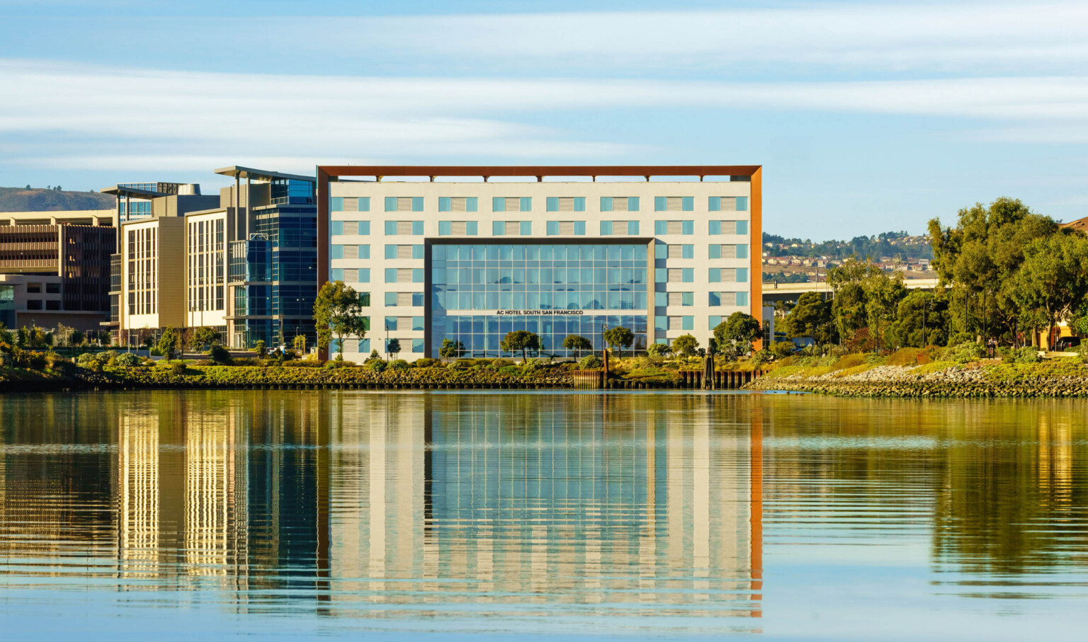 View of hotel entry across the water. The 7 story building has recessed section of floor to ceiling windows at center
