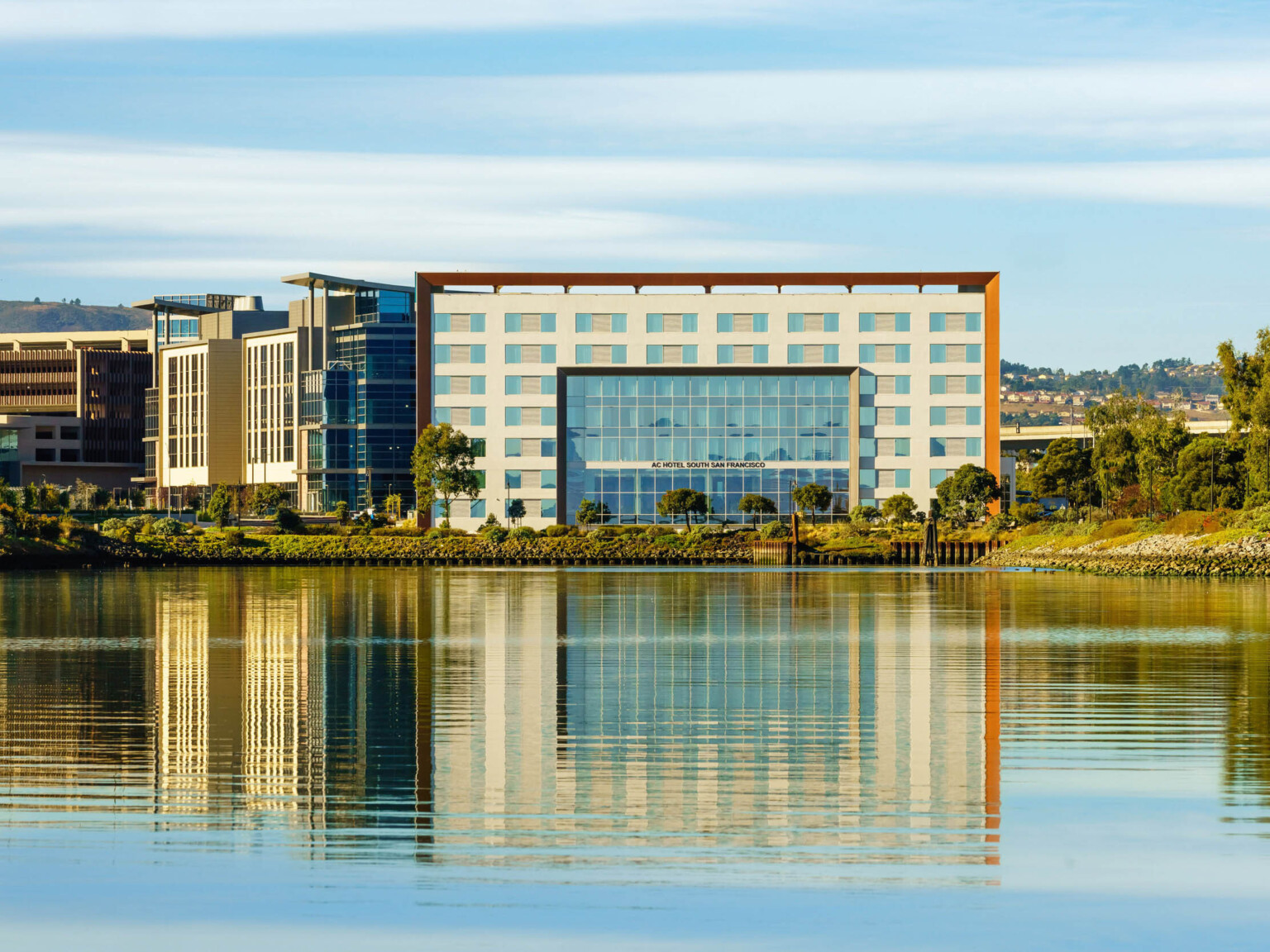 View of hotel entry across the water. The 7 story building has recessed section of floor to ceiling windows at center