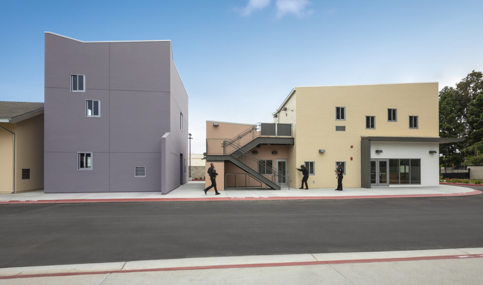 Officers participate in hands on scenario training at peach colored two story lab building with stairwell in front