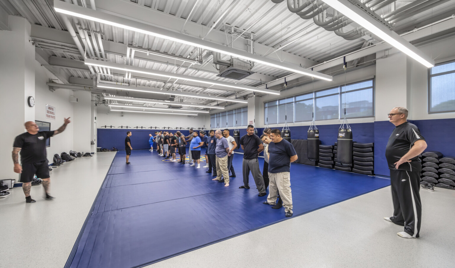 Exercise room with blue padding along floors and walls, men stand practicing at the center of the room with equipment behind