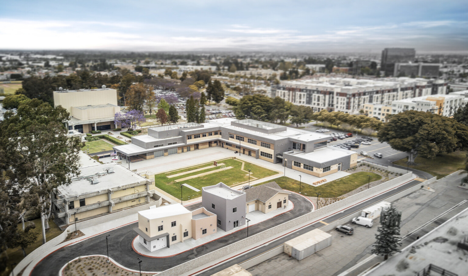 Aerial view of multi building complex from the rear with field at center