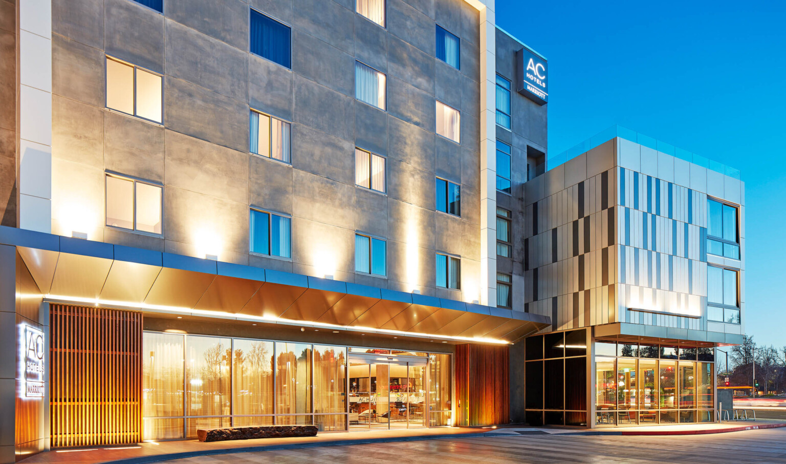 Sliding door entry to hotel illuminated from recessed light in overhang. Stone building with wood panels at bottom corners