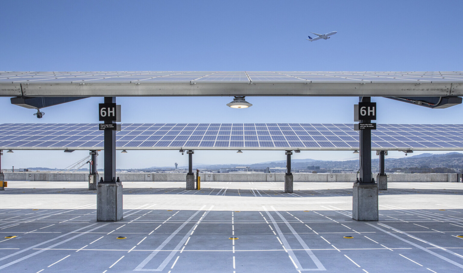 Rows of solar canopies over electric vehicle charging stations on roof of garage with view of mountains behind