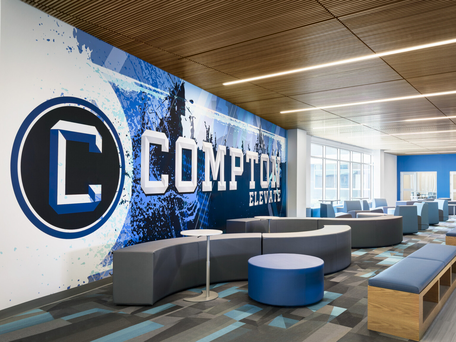 Common area of Compton High School; blue and white graphic design feature wall with "Compton" highlighted; community based-design seating