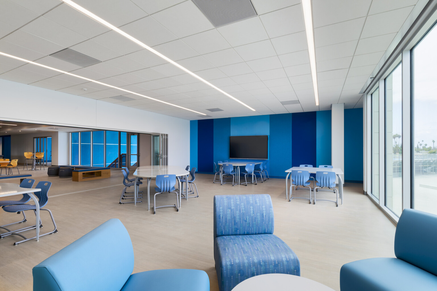 Compton High School common space with varying blue color wall features and blue tables; chairs and comfortable lounge chairs
