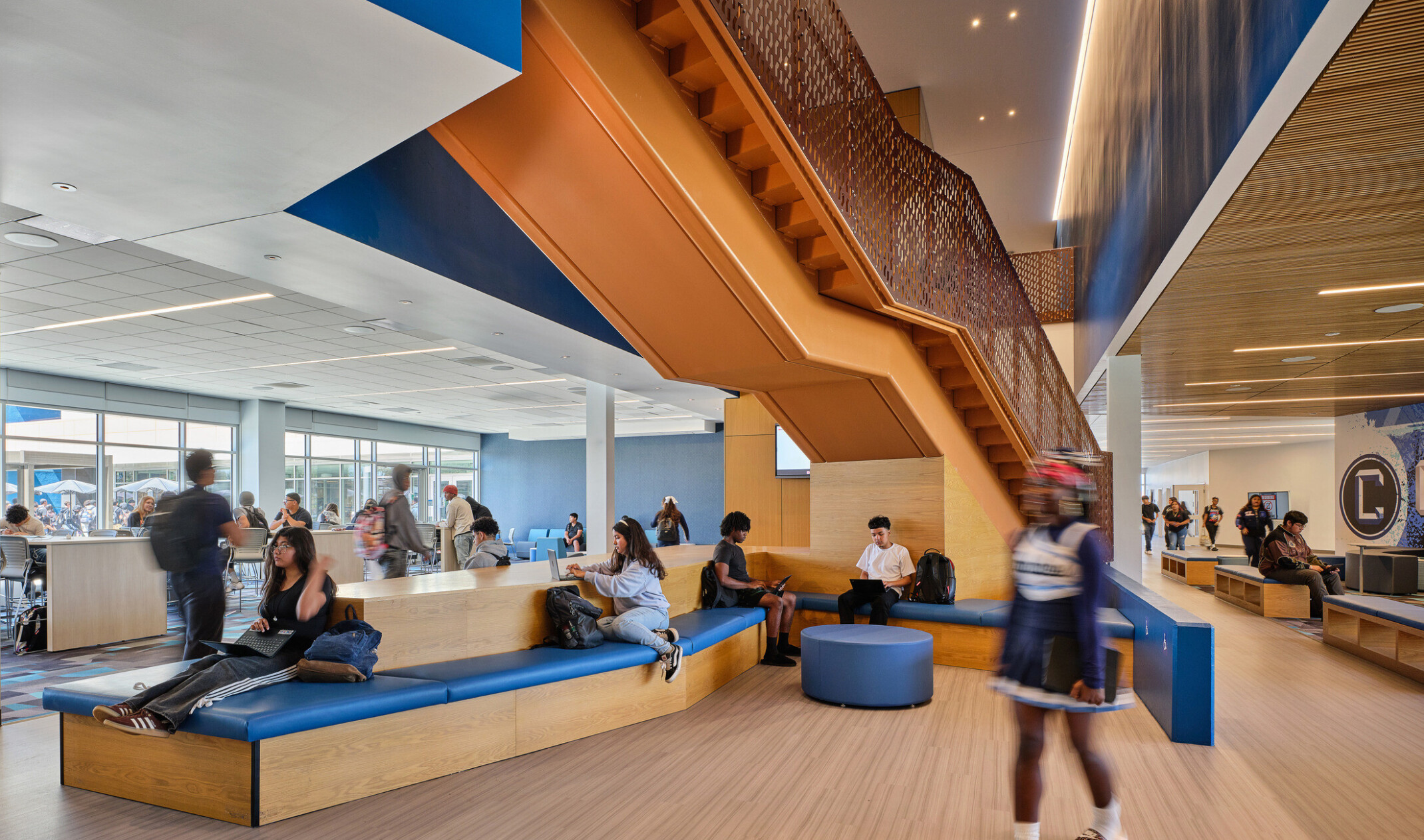 Students in a collaboration breakout space; modular desking and seats; blue and white accents against light wood; naturally lit space; Compton High School