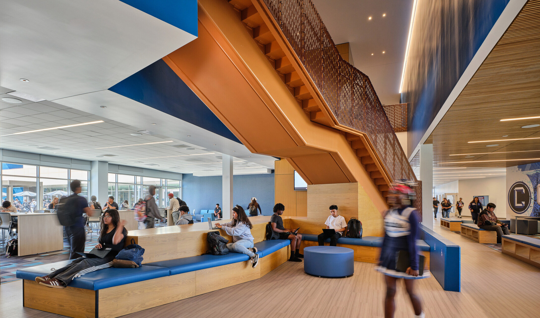Students in a collaboration breakout space; modular desking and seats; blue and white accents against light wood; naturally lit space; Compton High School