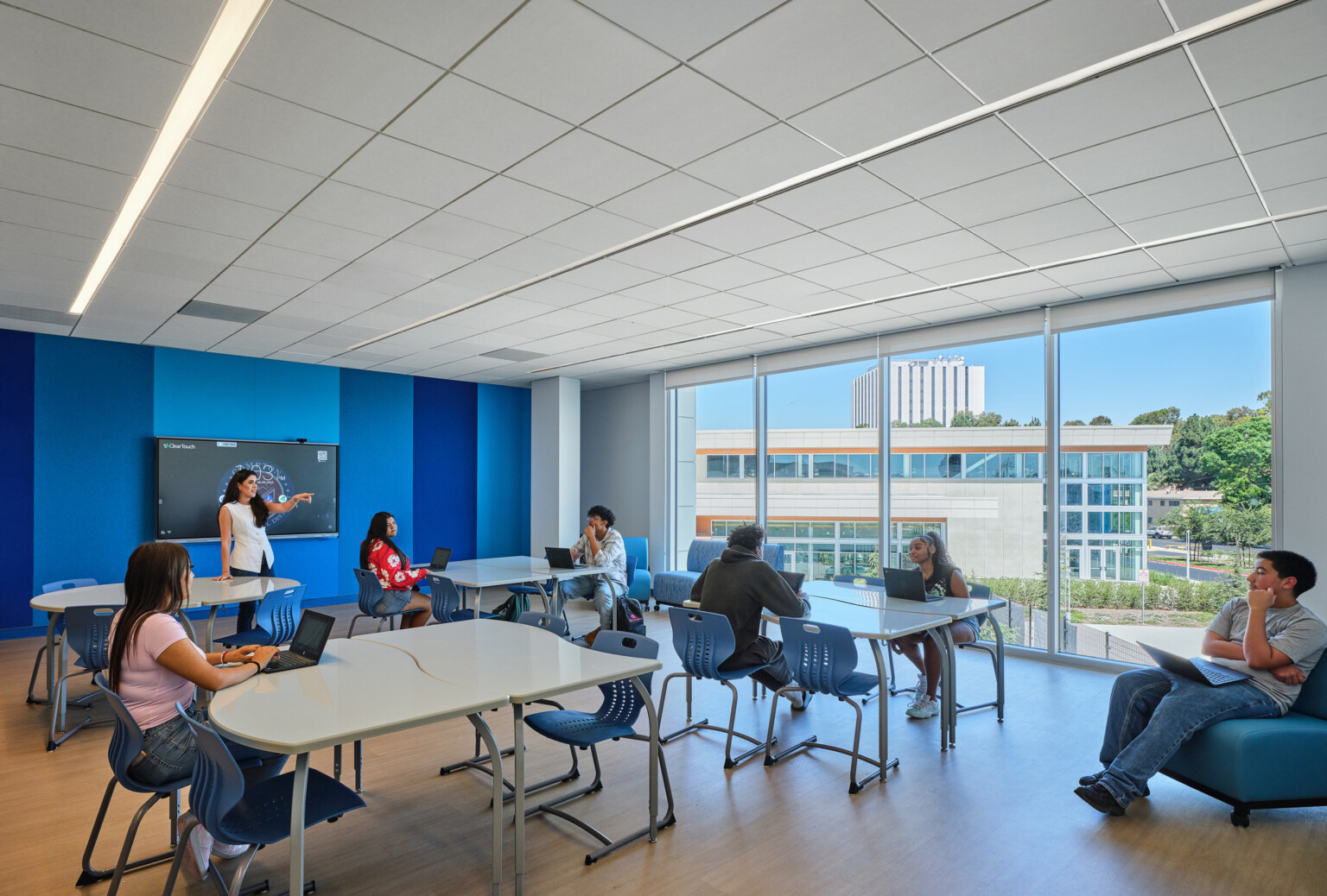 Classroom filled with students at tables collaborating and working; blue and white accents on the floor and walls; Compton High School