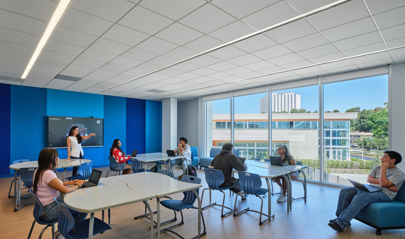 Classroom filled with students at tables collaborating and working; blue and white accents on the floor and walls; Compton High School