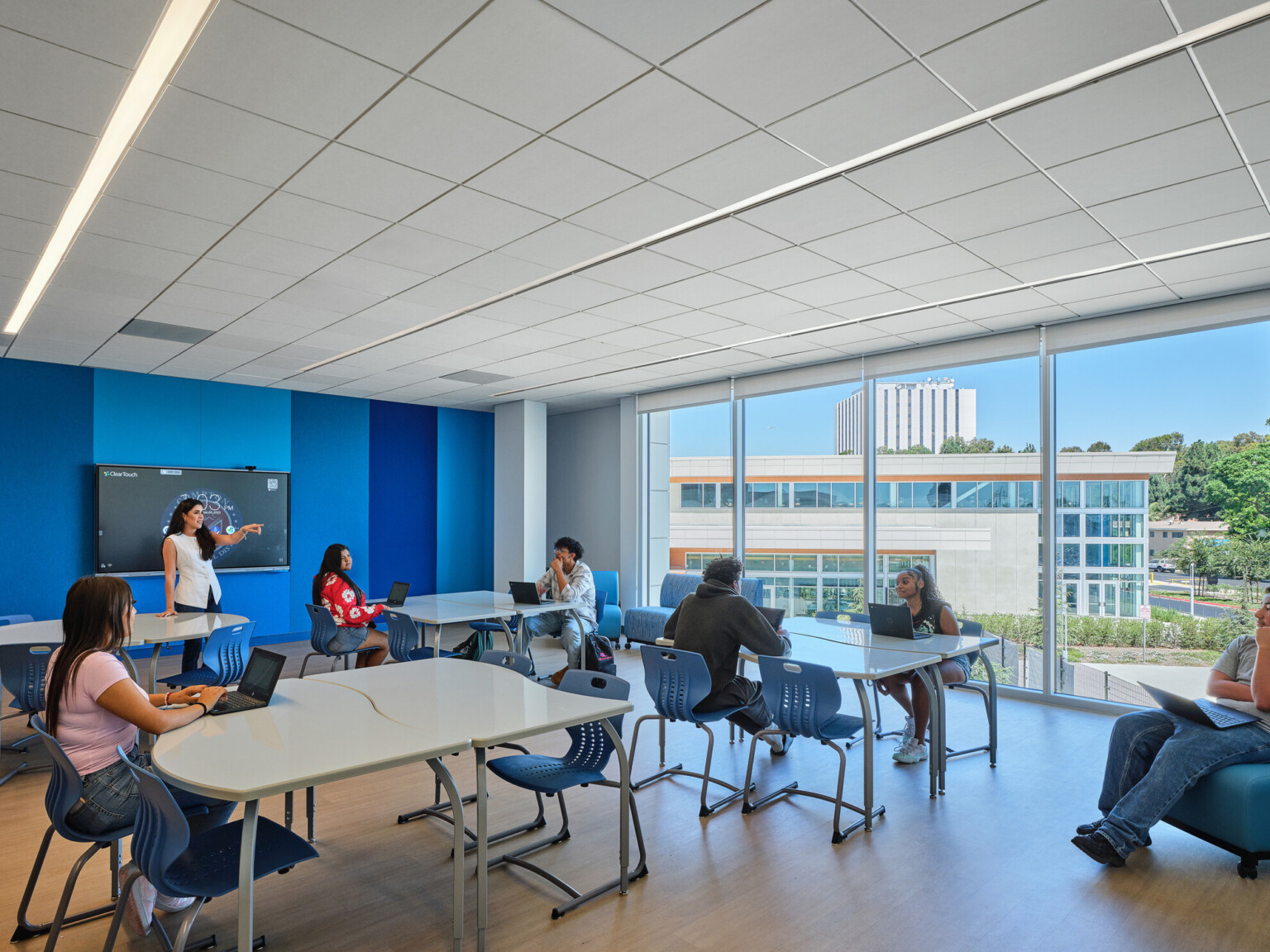 Classroom filled with students at tables collaborating and working; blue and white accents on the floor and walls; Compton High School