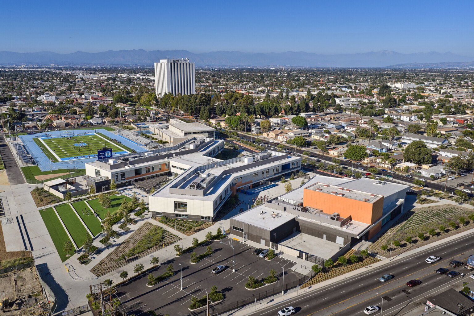 Compton High School; orange sign with the name, modern facade and greenery in front of blue skies; community neighborhood design