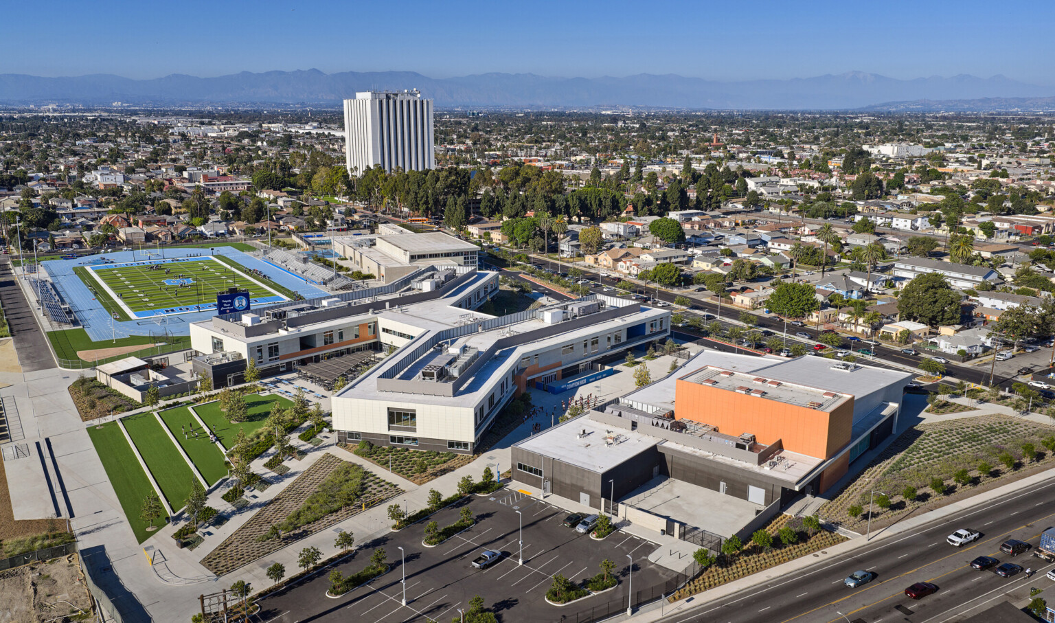 Compton High School; orange sign with the name, modern facade and greenery in front of blue skies; community neighborhood design