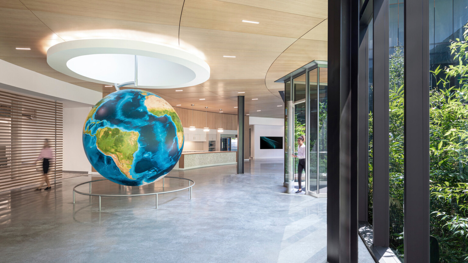 Curved hallway with floor to ceiling windows and wood panel ceiling. Round white recessed ceiling detail with hanging globe