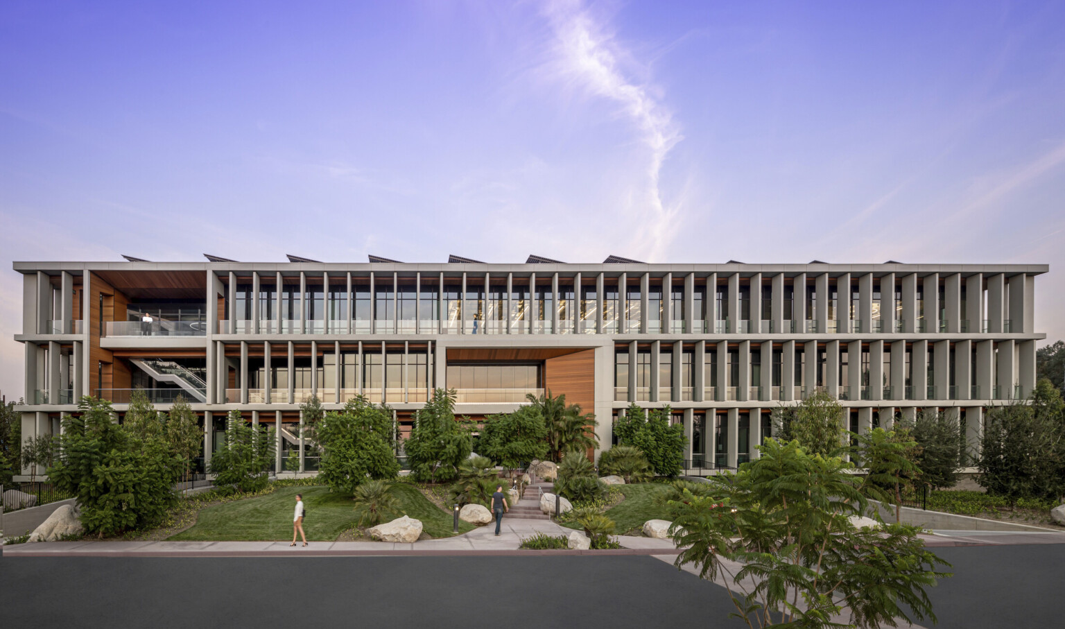 White wrapped slat facade with wood accents over above grade glass building. Lawn with large plants slopes up to building