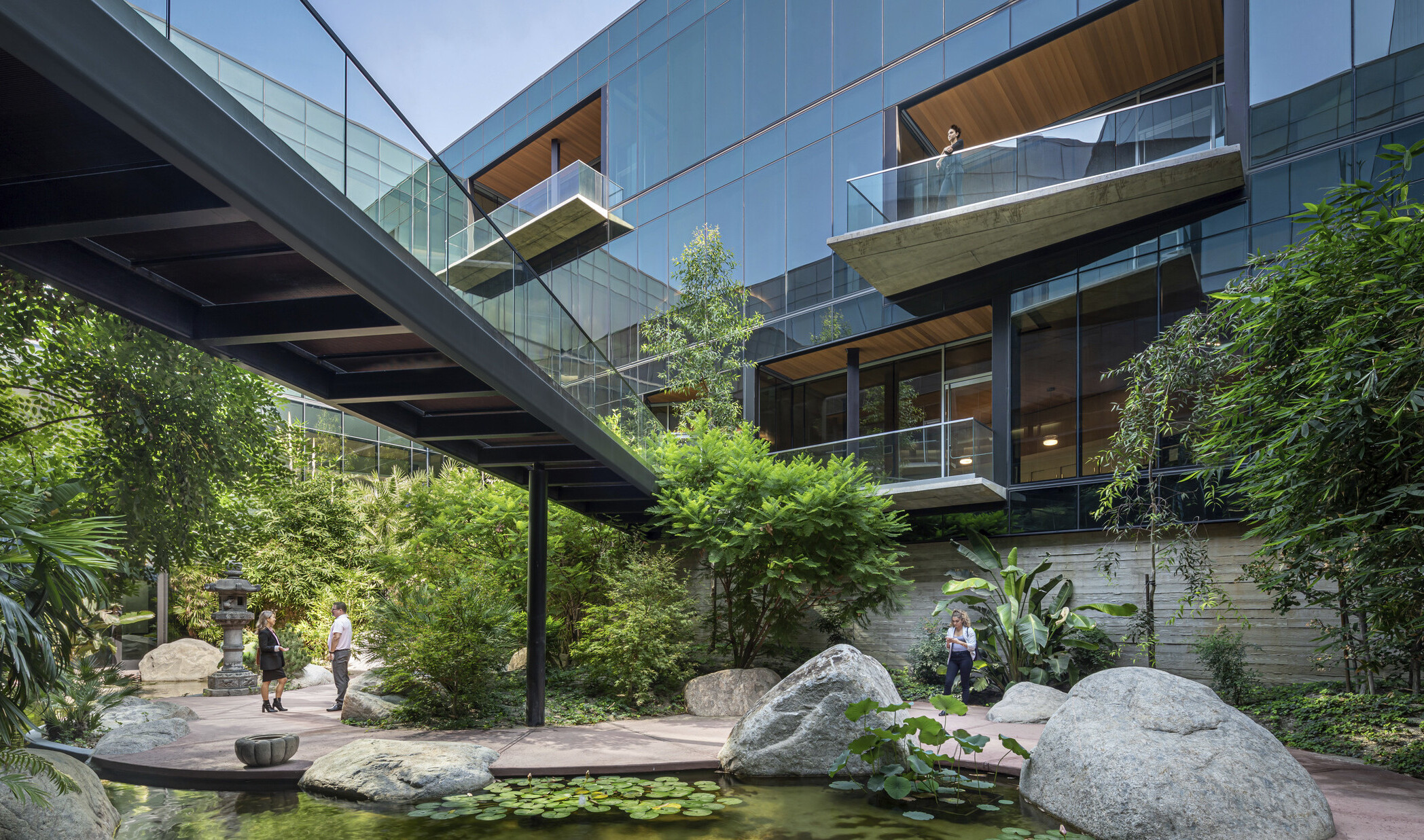 ESRI Campus front courtyard expansion. Angled overhanging balconies on a glass building with bridge over courtyard garden