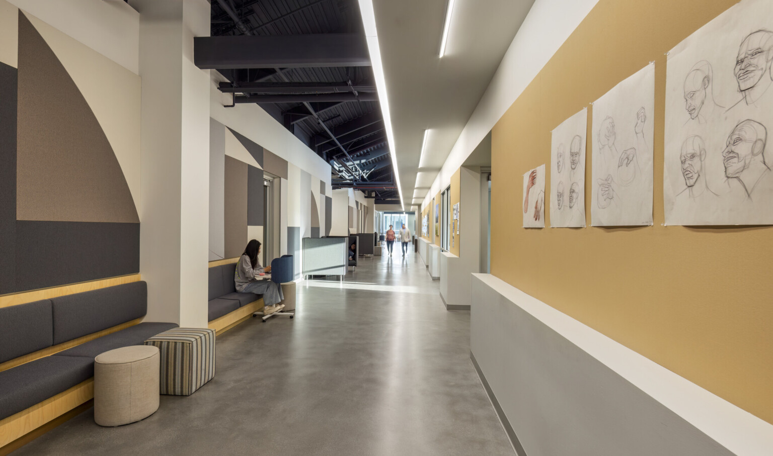hallway in the Irvine Valley College Fine Arts Building; grey floors and light tan accents make for a modern space with seating and student designs on the opposing walls