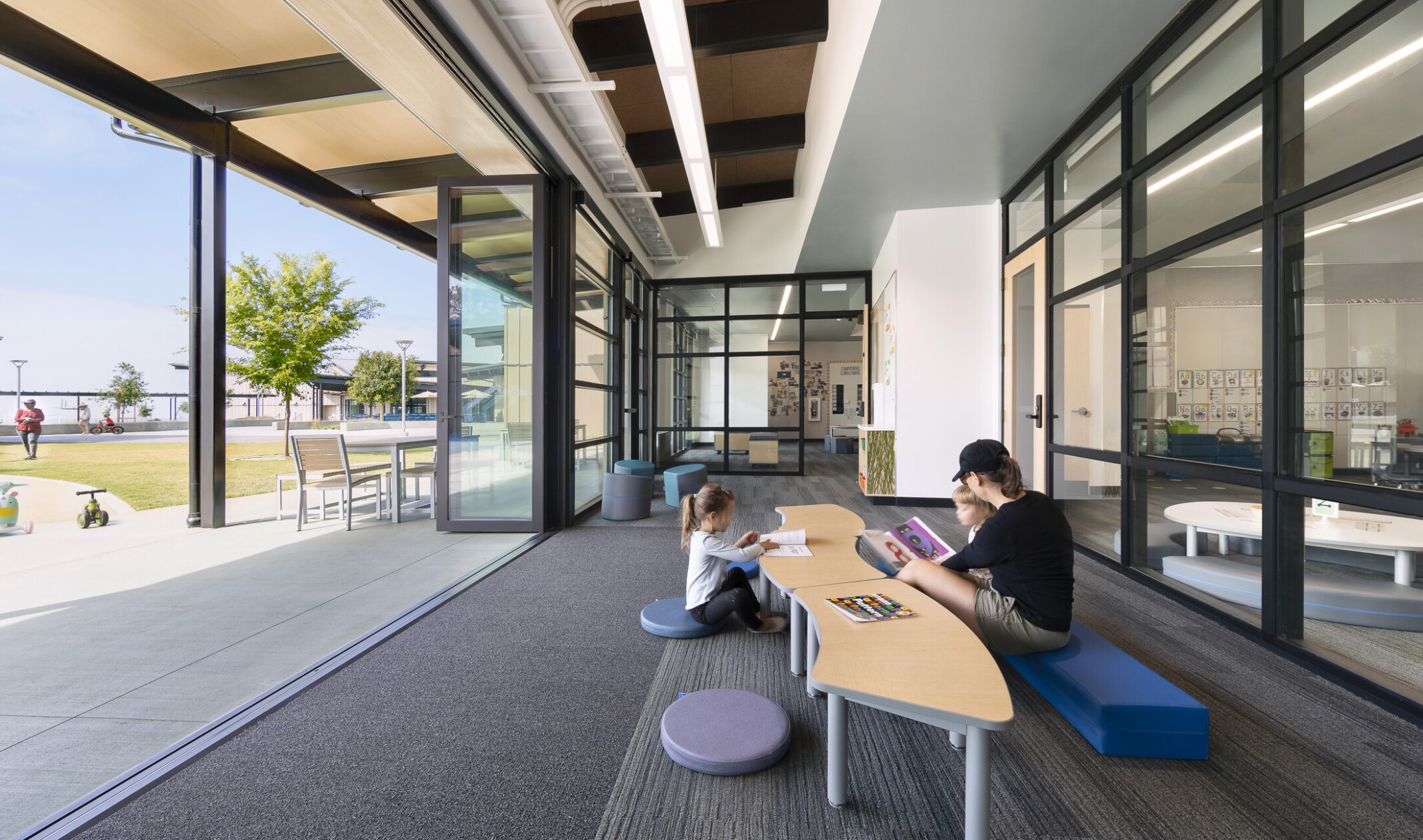 exterior of Del Mar Heights School; indoor outdoor learning space with large openable windows; tables for community learning and teaching; black metal trim lines the building and windows of the building