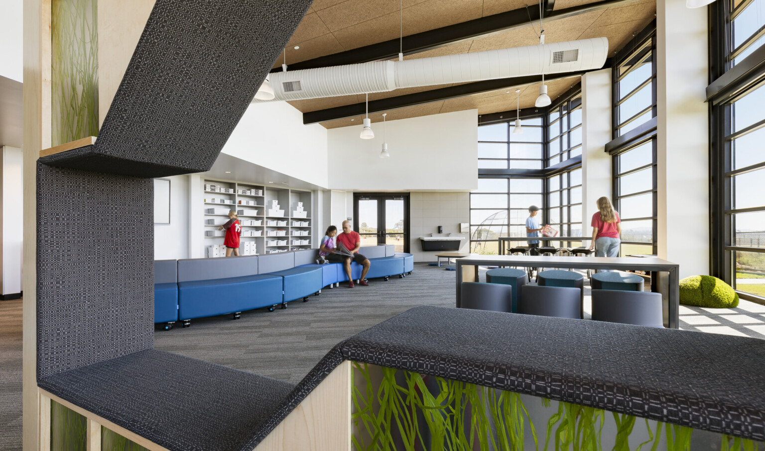 library of Del Mar Heights School; indoor outdoor learning space with large floor to ceiling windows; coastal community design with sand and wood tones with greenery; children reading in shelves with benches build into them