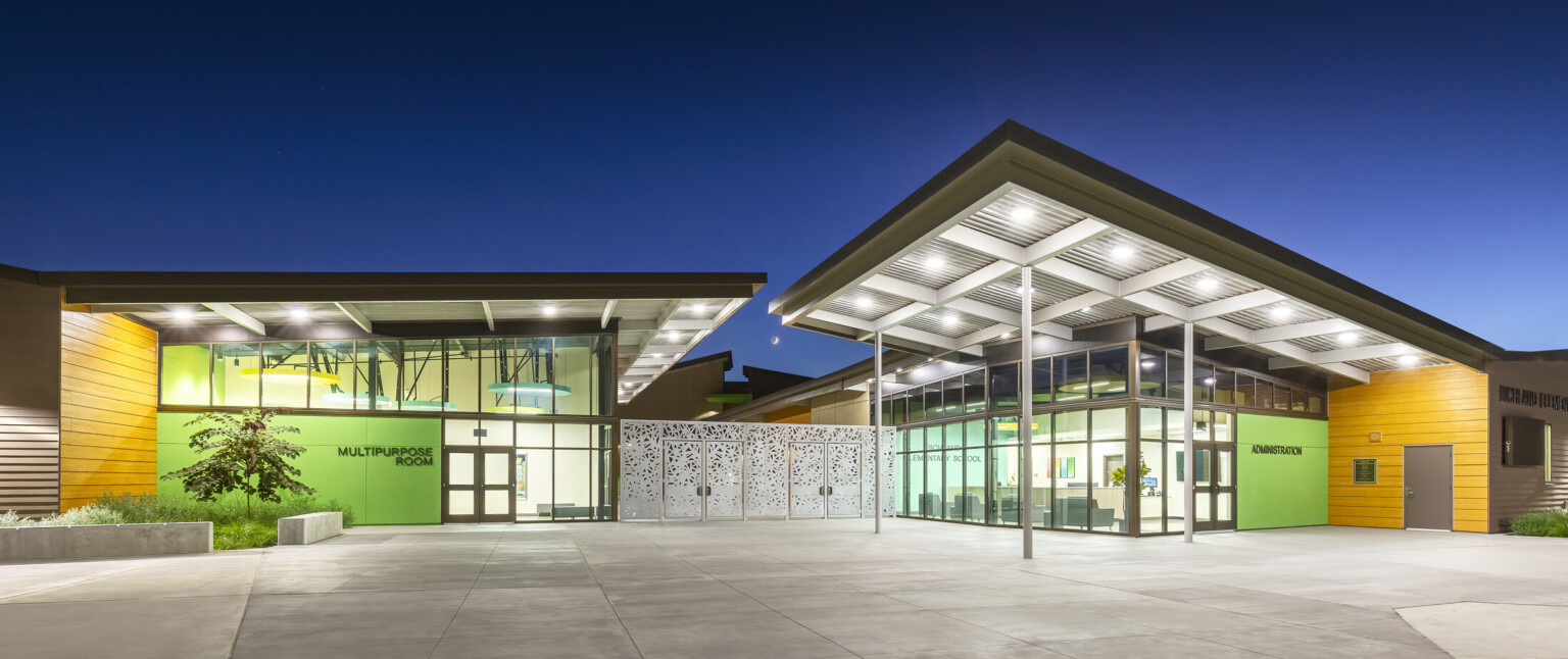 Canopy over building exterior entrance patio illuminated in the evening, large floor to ceiling windows