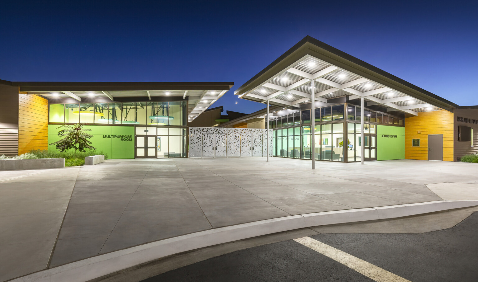 Canopy over Richland Elementary School exterior entrance patio illuminated in the evening; large floor to ceiling windows