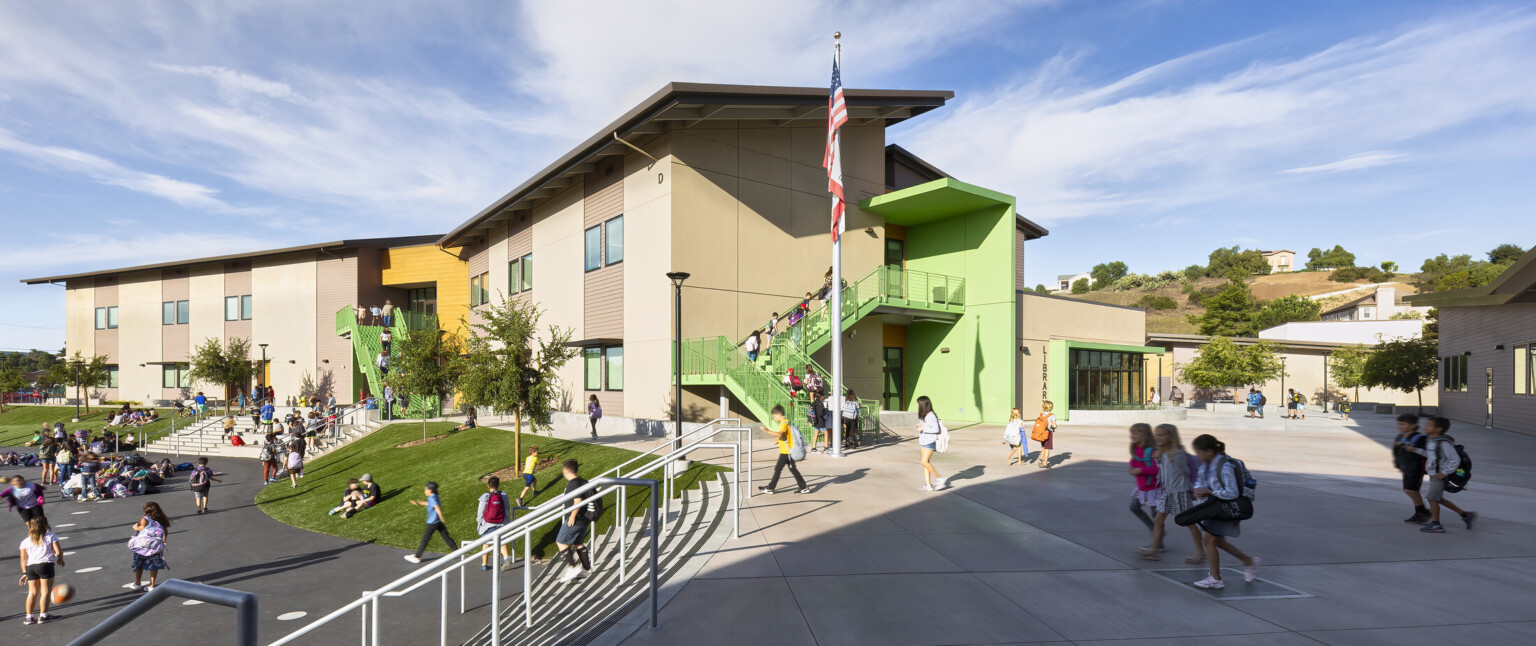 Exterior partially shaded courtyard with steps to playground, multistory buildings on elementary school campus