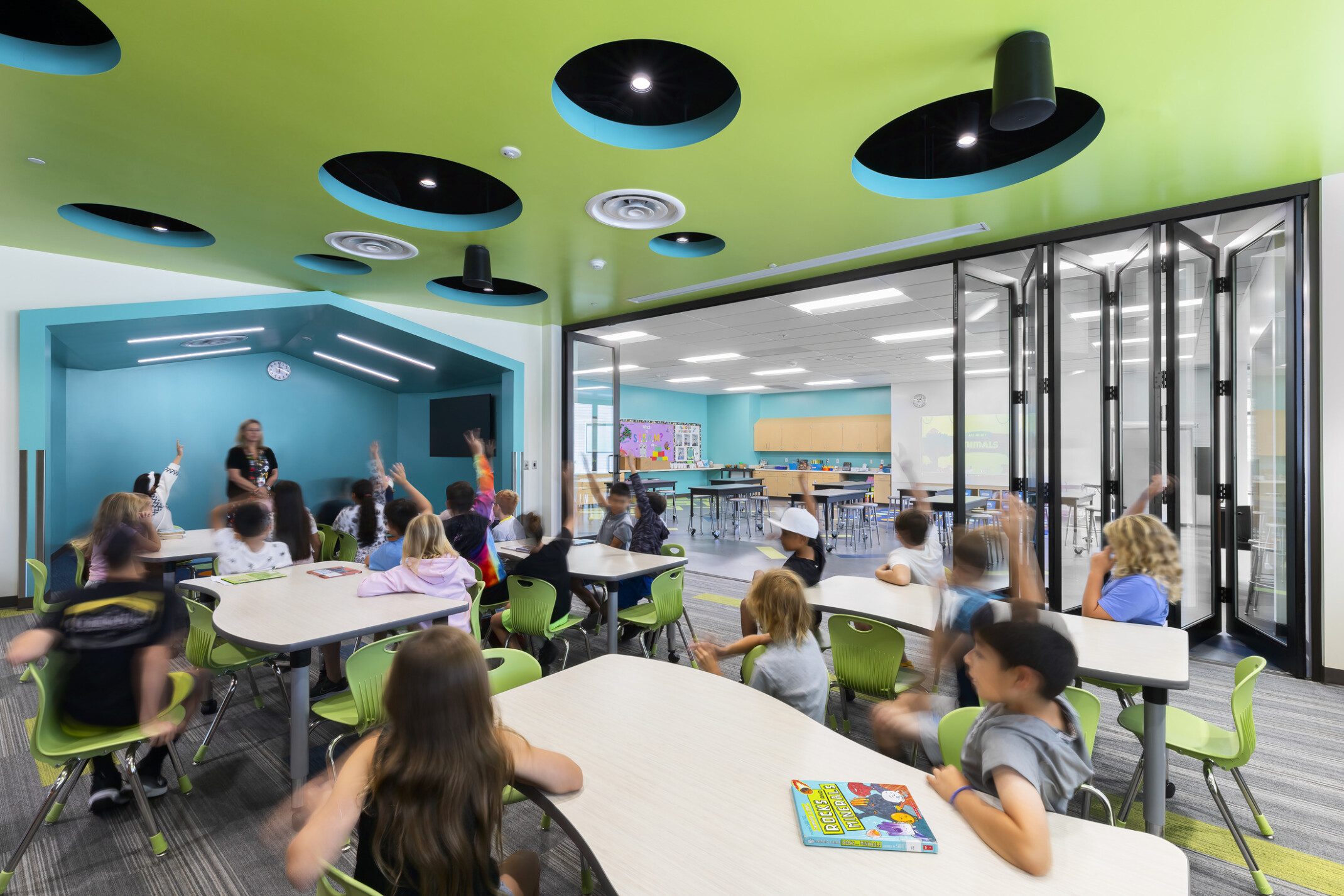 Richland Elementary School flexible learning space; collapsible glass walls, green ceiling; blue accents, dimensional recessed lights; modern campus design with bright colors; pod table formation