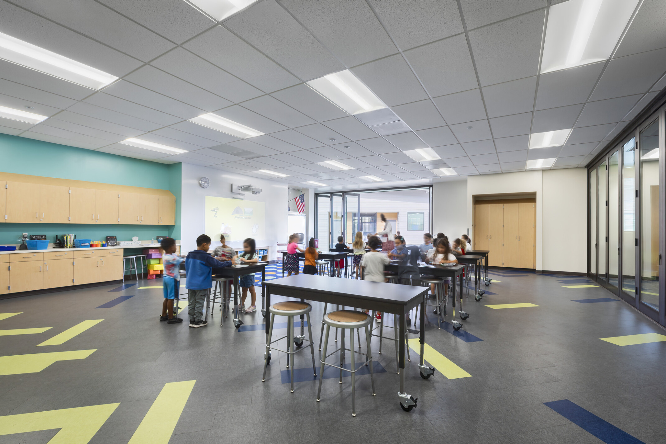 Richland Elementary School learning space with bright color accents; flexible glass walls students works at tables; stools; campus design with open entrance to hallway