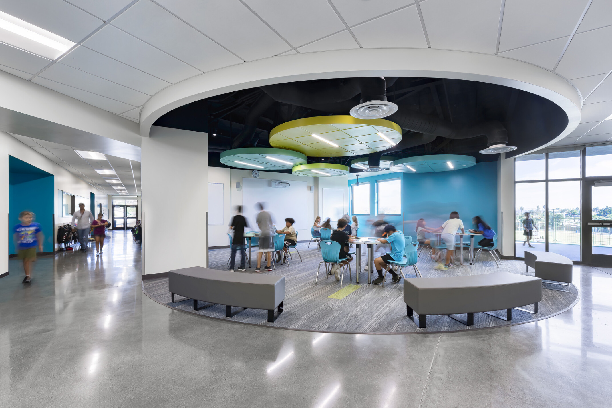 Richland Elementary School; central common area recessed from main hallway; shades of blue on wall and flexible seating; learning spaces pods; floor to ceiling windows