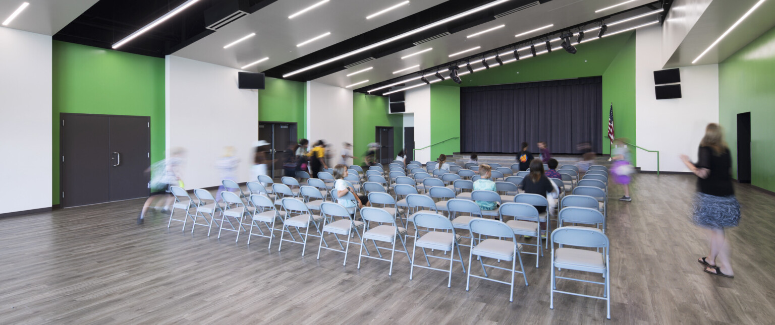 Auditorium with folding chairs facing small black stage bright green wall accents