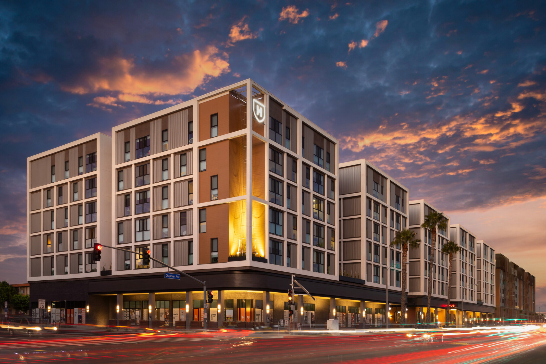 Dusk exterior view of Hub Fullerton's west corner, photographed from the opposite side of the street, with the building's full length visible toward the east corner.