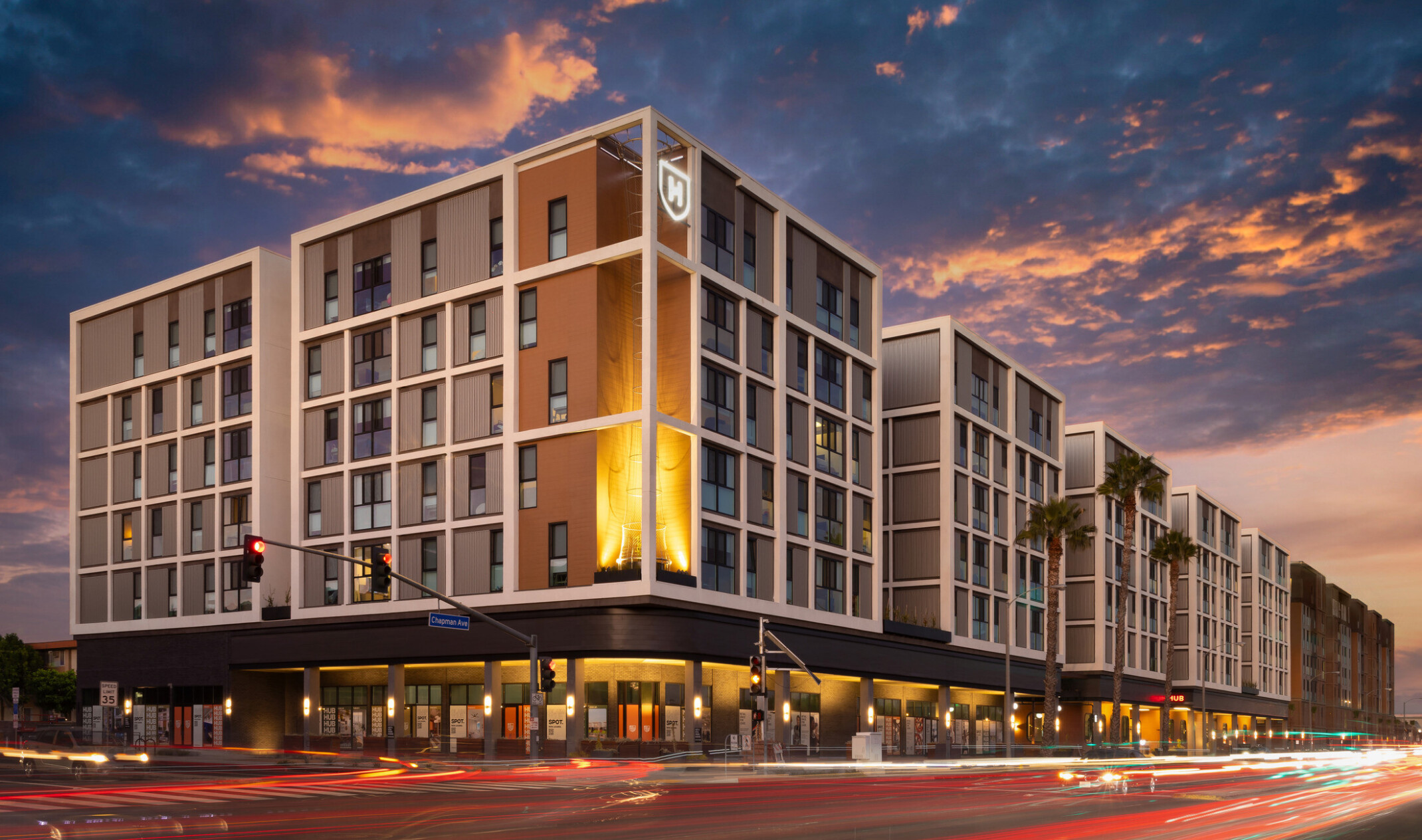Dusk exterior view of Hub Fullerton's west corner, photographed from the opposite side of the street, with the building's full length visible toward the east corner.