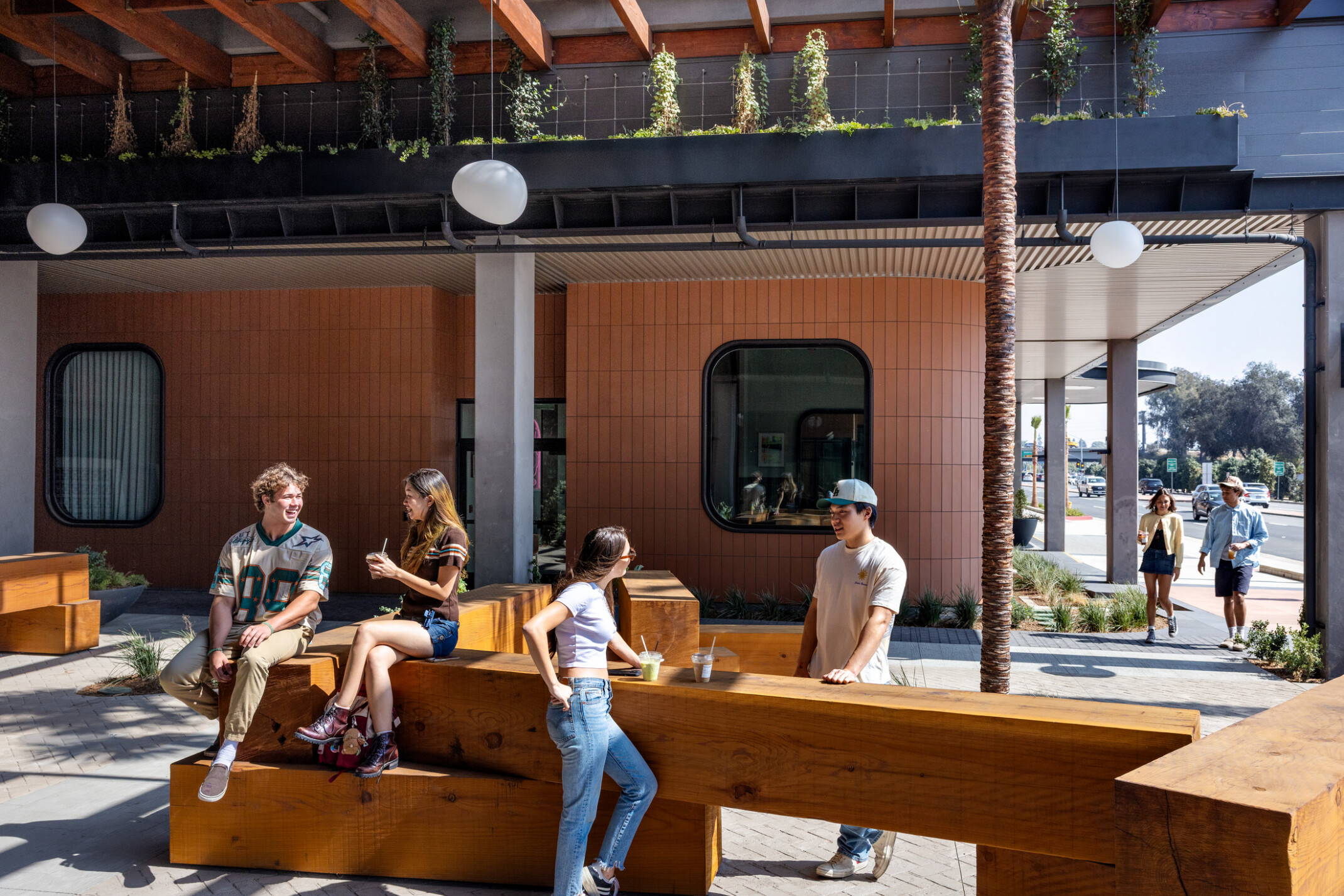 Students sitting on stacked square timber blocks in Hub Fullerton's paseo, drinking beverages.