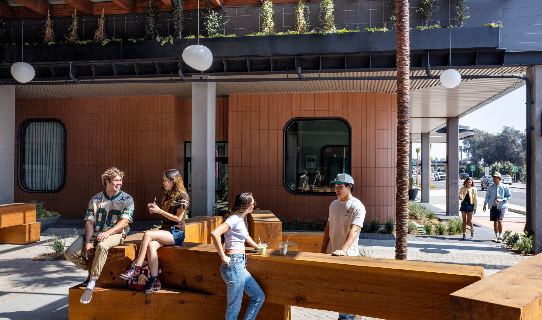 Students sitting on stacked square timber blocks in Hub Fullerton's paseo, drinking beverages.