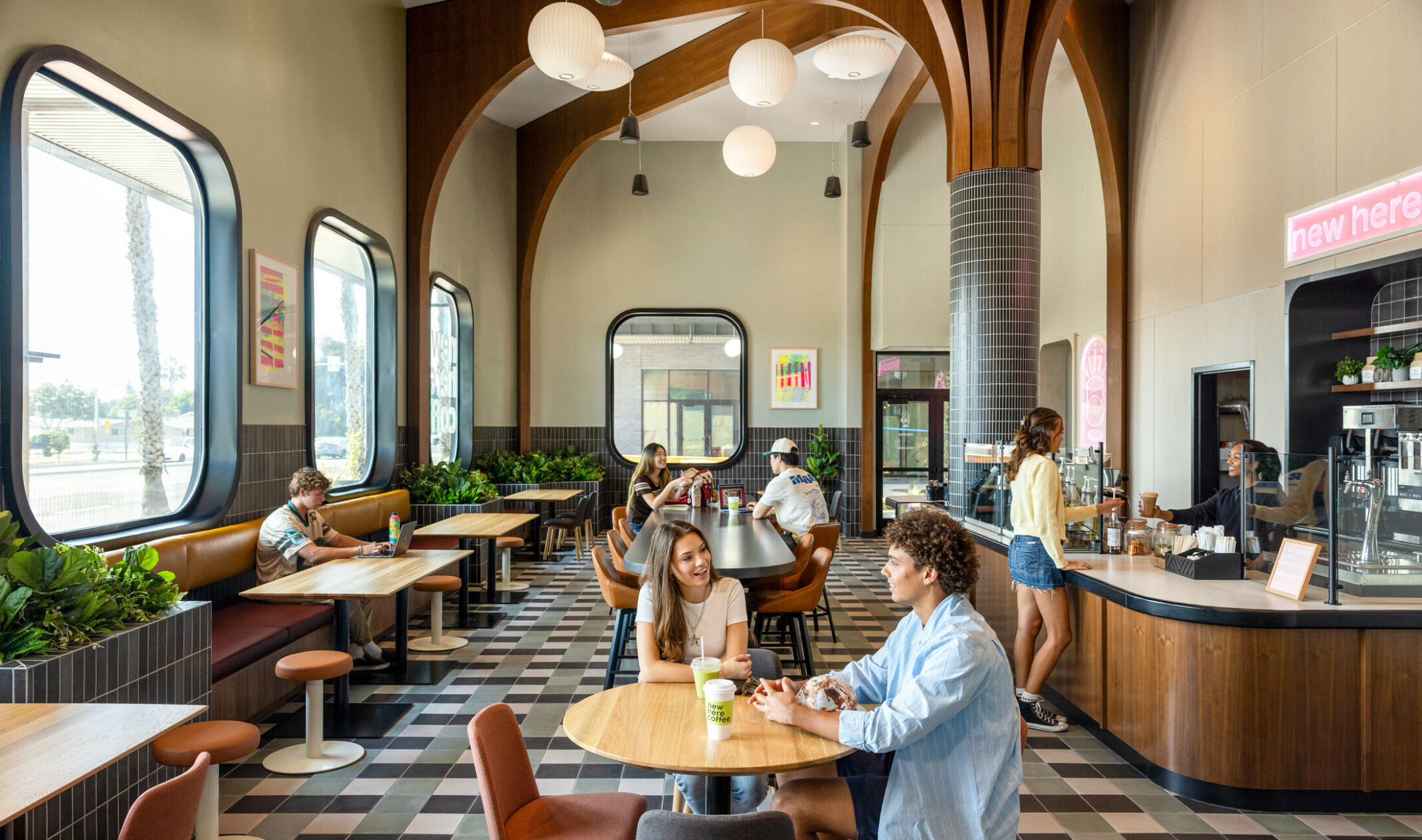 Interior view of Hub Fullerton's coffee shop, with students studying alone in a booth, others chatting at a table, and a customer ordering a drink at the counter.