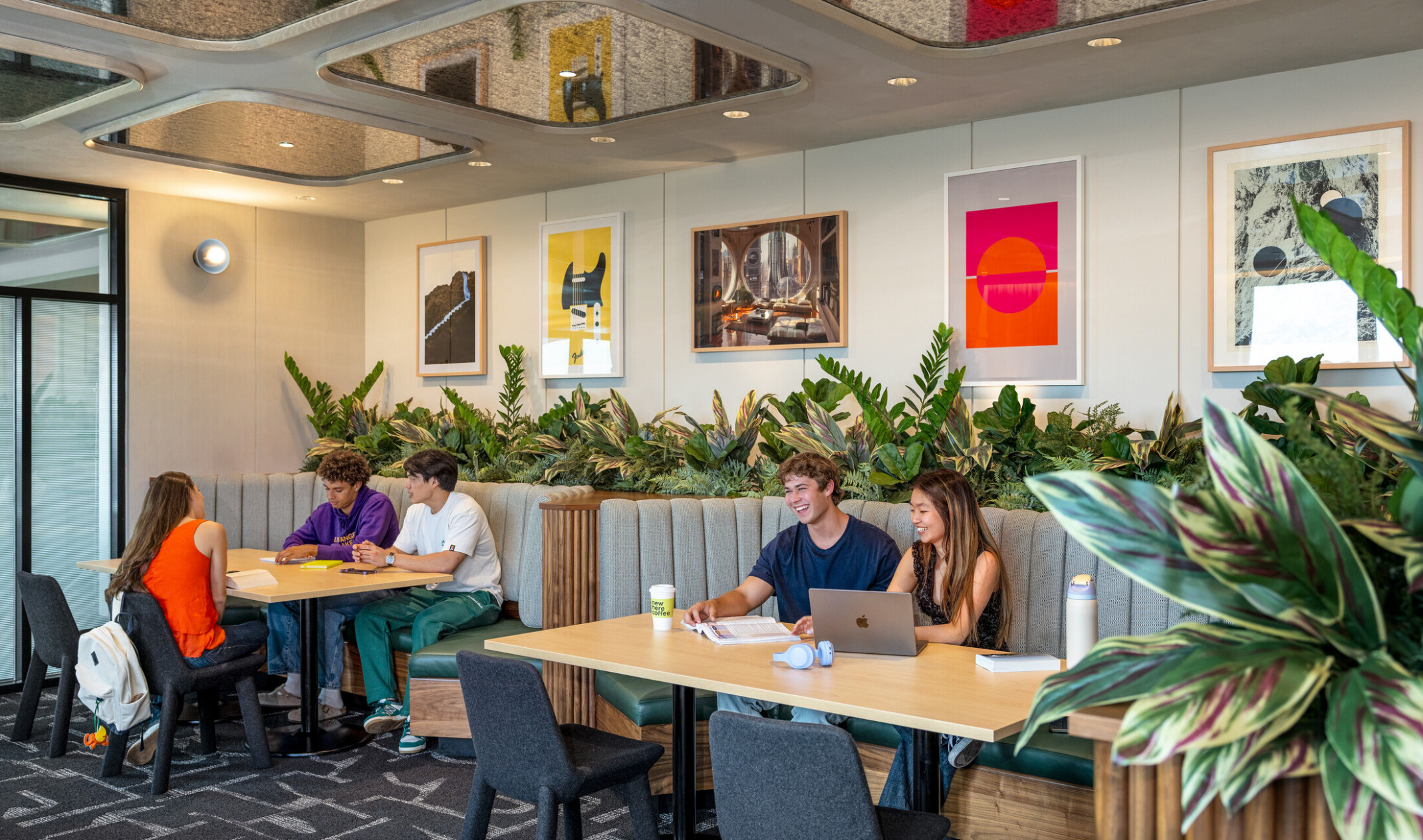 A study lounge at Hub Fullerton, with plant-surrounded booths, framed artwork on the walls, and distressed mirror accents overhead.