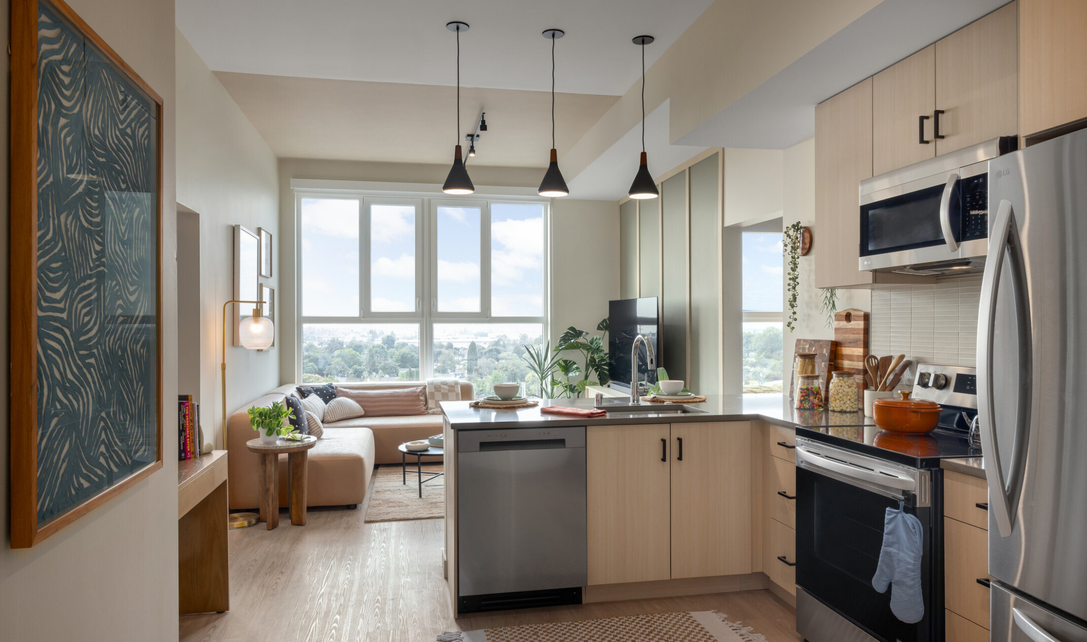Interior view of a fully furnished Hub Fullerton unit, looking from the kitchen through the living room toward the windows.