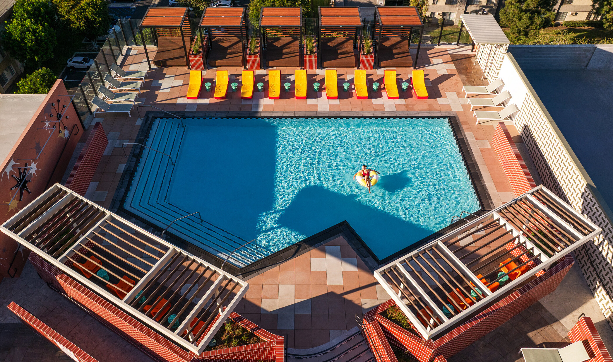 Aerial view of Hub Fullerton's rooftop pool, with cabanas and pool chairs lining the deck and one person floating on a tube in the pool.