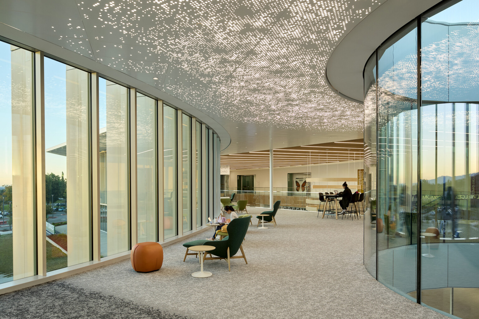 image of a college seating area; overlooking the floor to ceiling windows; man sitting and studying at comfortable chairs