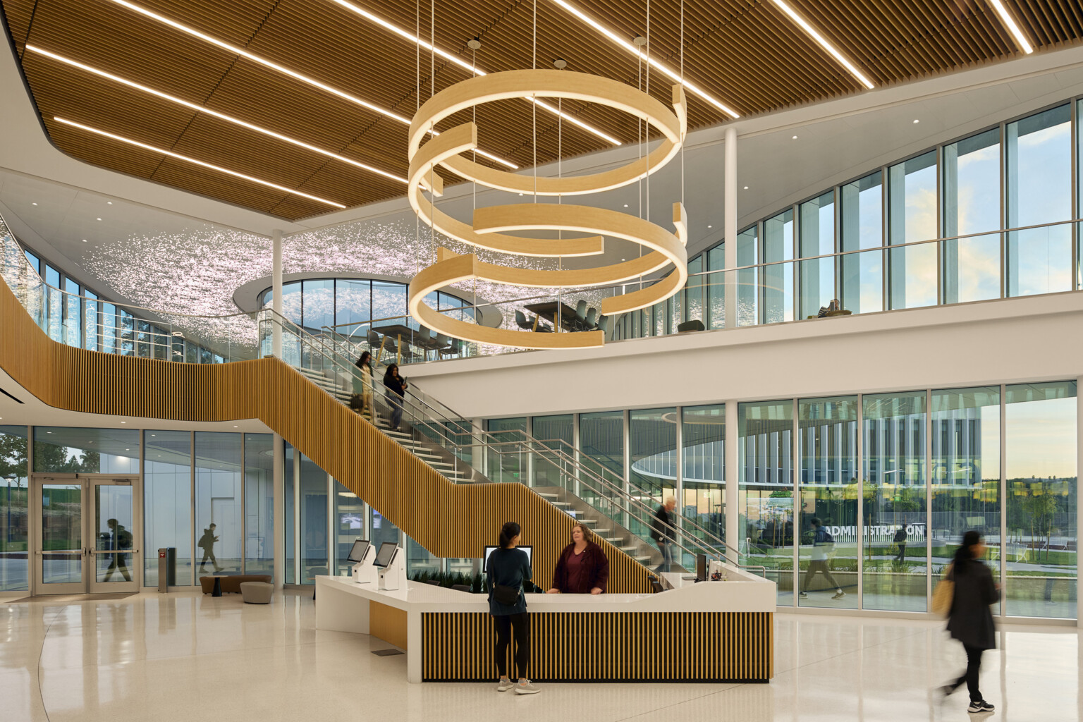 large double height atrium lobby area with feature circular lighting; floor to ceiling windows; natural palette of materials decorate space