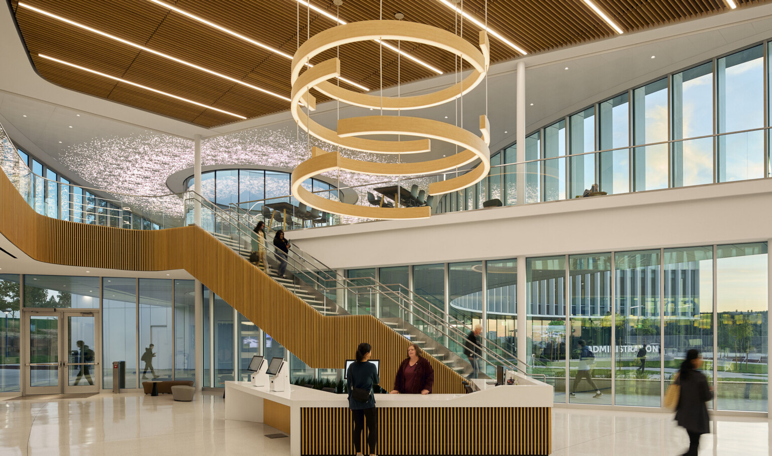 large double height atrium lobby area with feature circular lighting; floor to ceiling windows; natural palette of materials decorate space