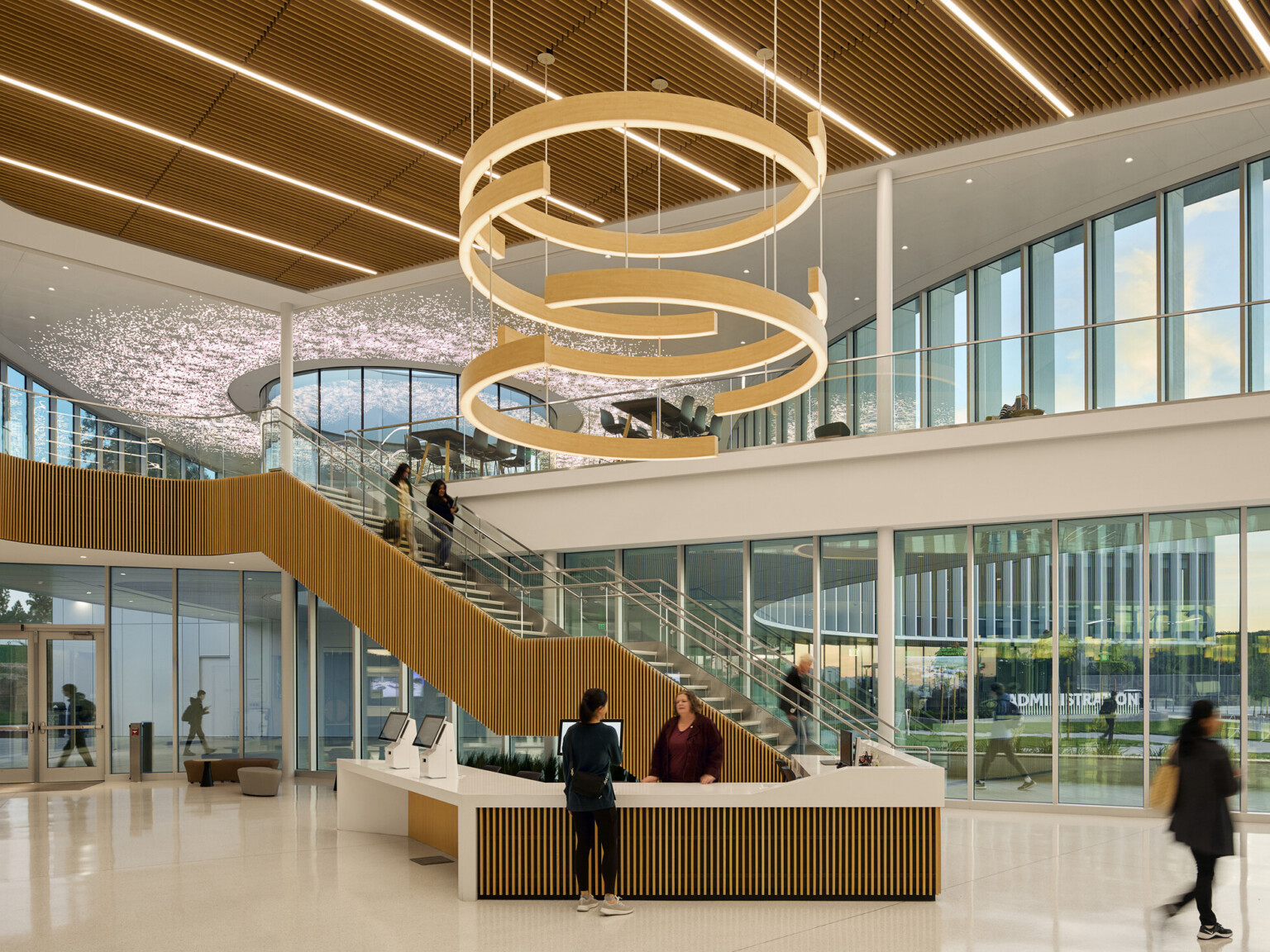 large double height atrium lobby area with feature circular lighting; floor to ceiling windows; natural palette of materials decorate space