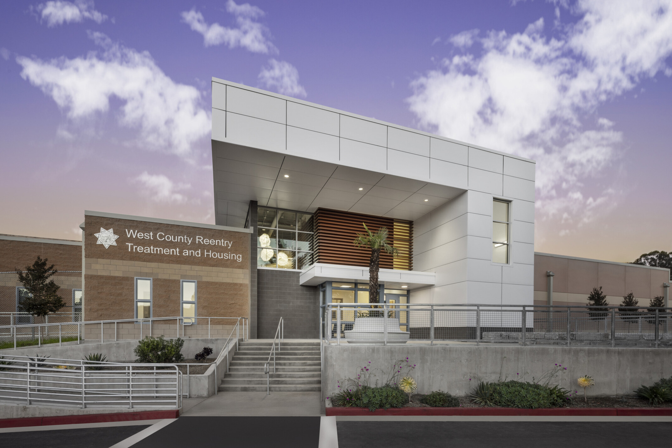 Primary entrance to West County Reentry Treatment and Housing; light brick facade and a white metal panel awning.