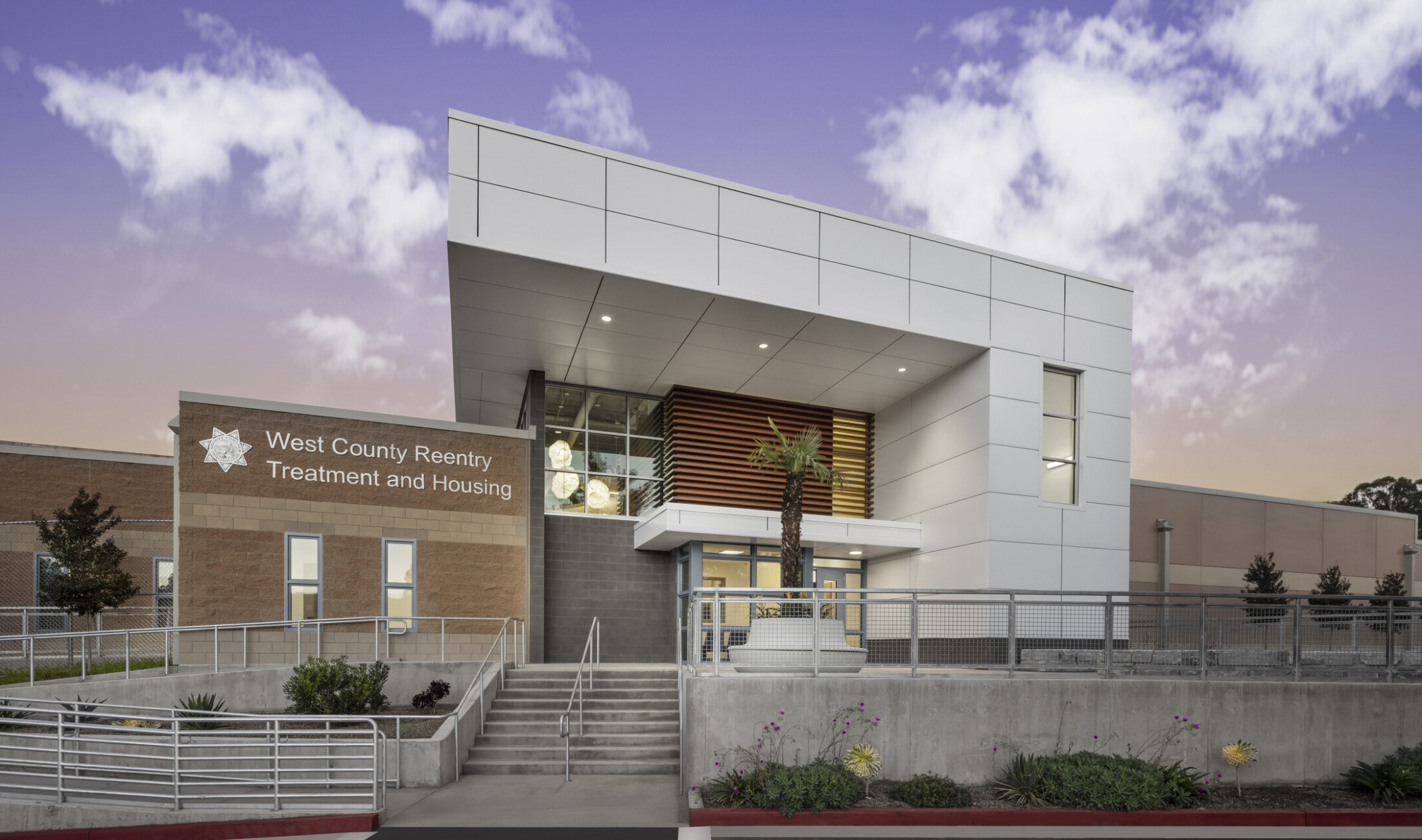 Primary entrance to West County Reentry Treatment and Housing; light brick facade and a white metal panel awning.