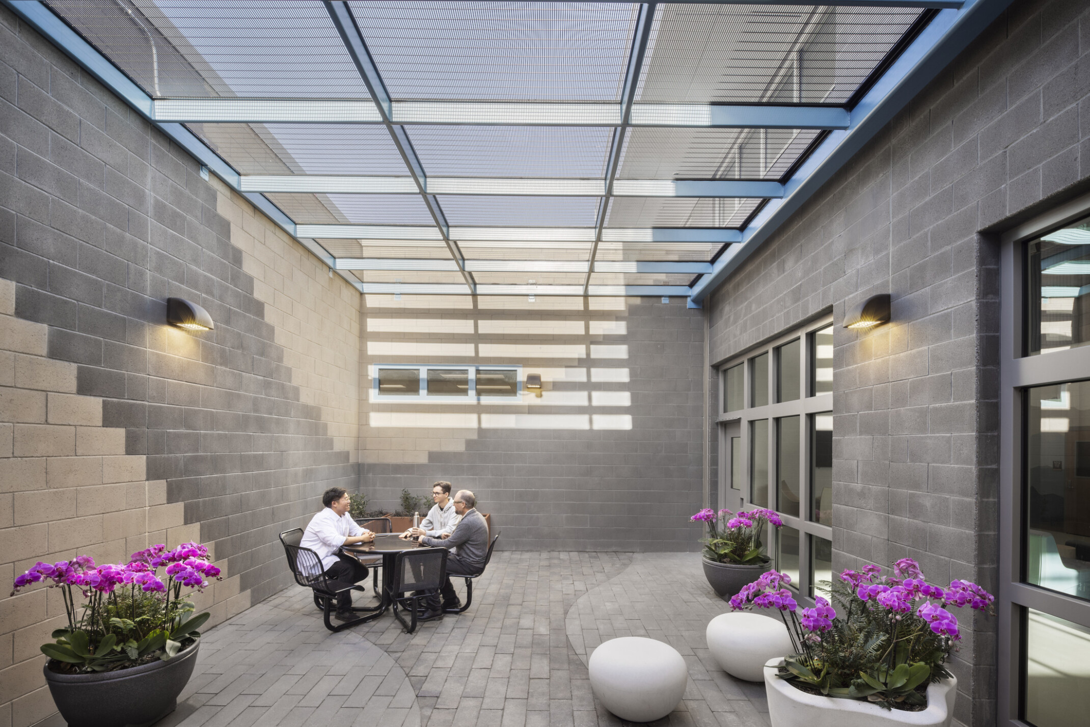 People sit at a round table in the outdoor visitation space, surrounded by light gray brick and flowerpots.