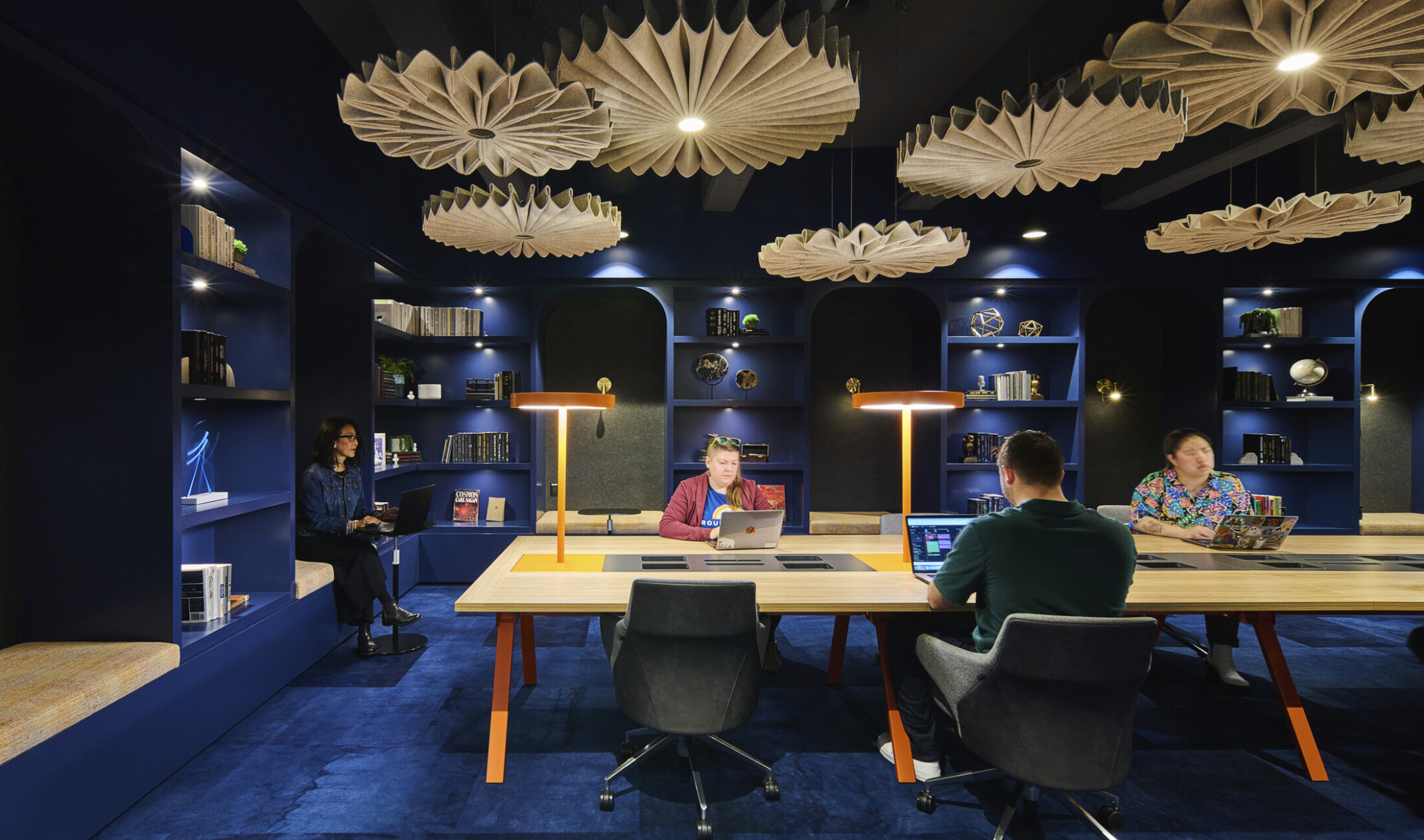 people working at a light wood table in a room with dark blue walls and ceilings, dark blue carpet and light wood chandeliers