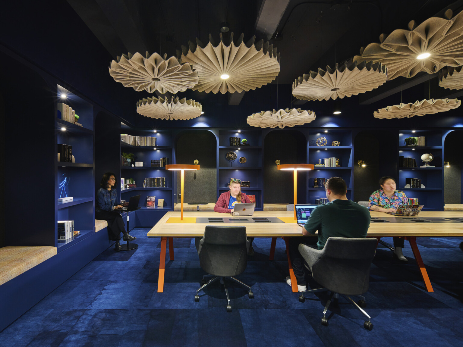 people working at a light wood table in a room with dark blue walls and ceilings, dark blue carpet and light wood chandeliers