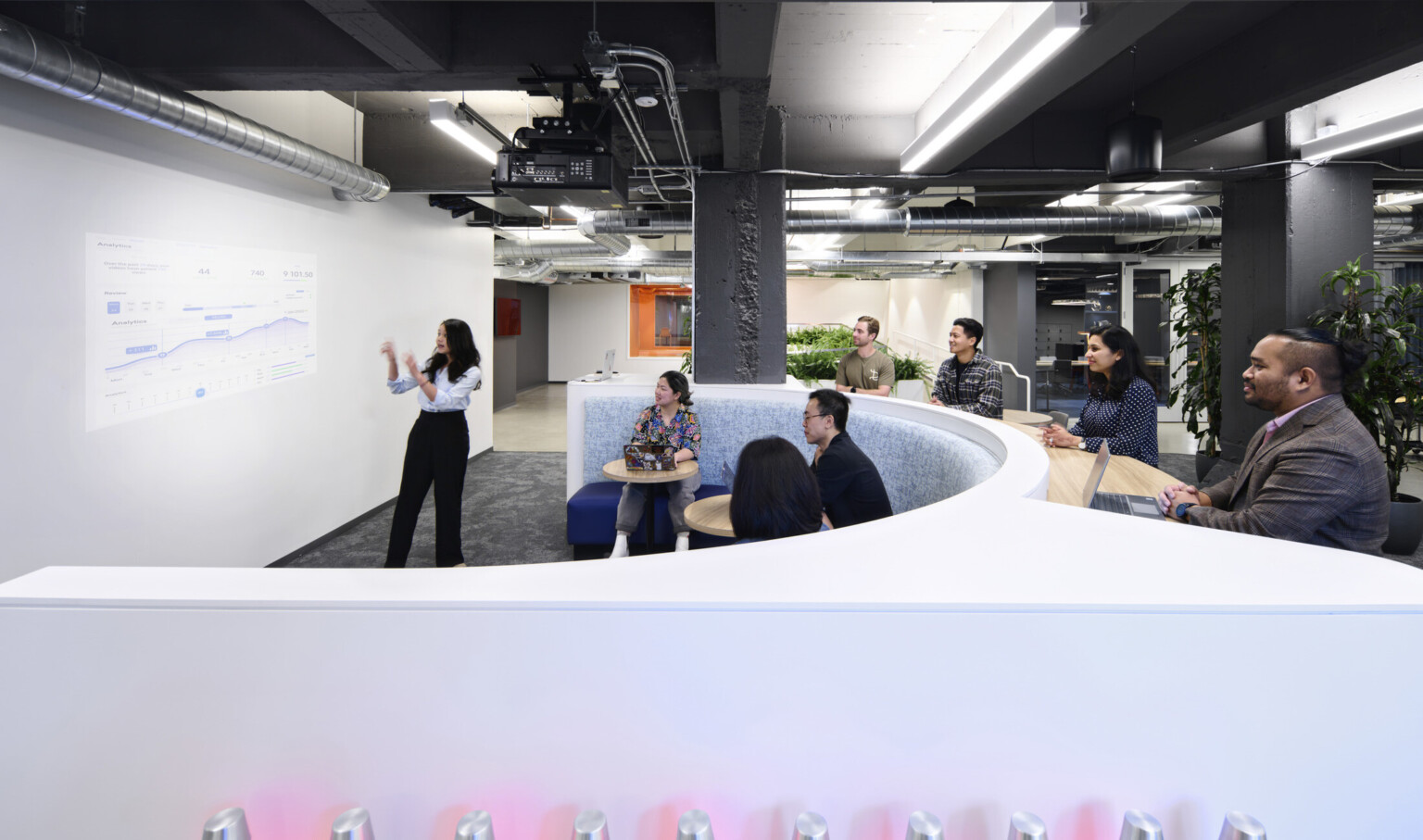 Rounded white desk with bench seating in front faces white board wall in open floor plan meeting space