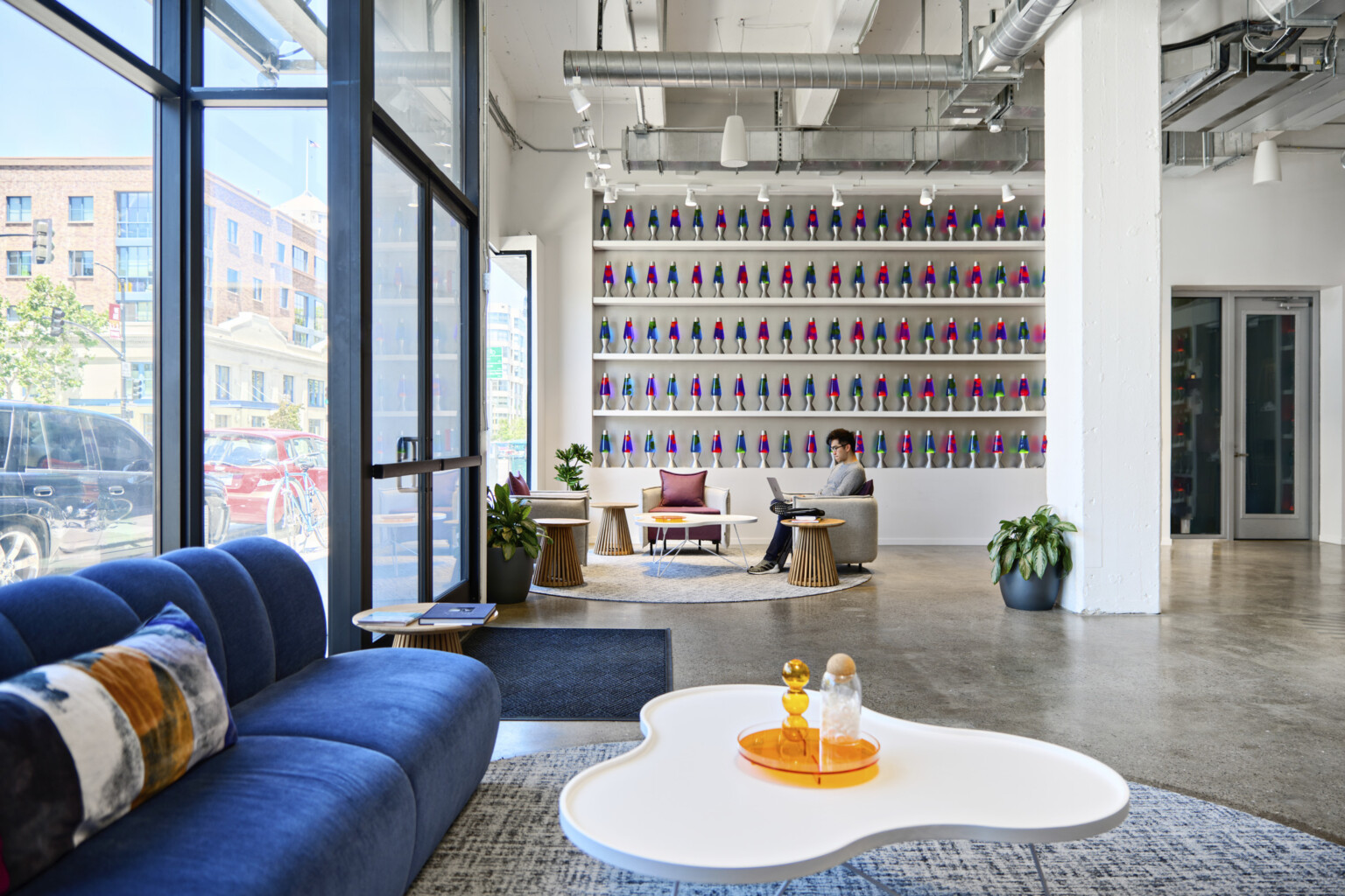 Cloudflare San Francisco Headquarters lobby with mixed comfortable seating and tall ceilings. Wall of blue and pink lava lamps on white built in shelves